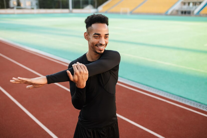young-attractive-smiling-african-american-sportsman-happily-stretching-preparing-run-racetrack-city-stadium_574295-3123